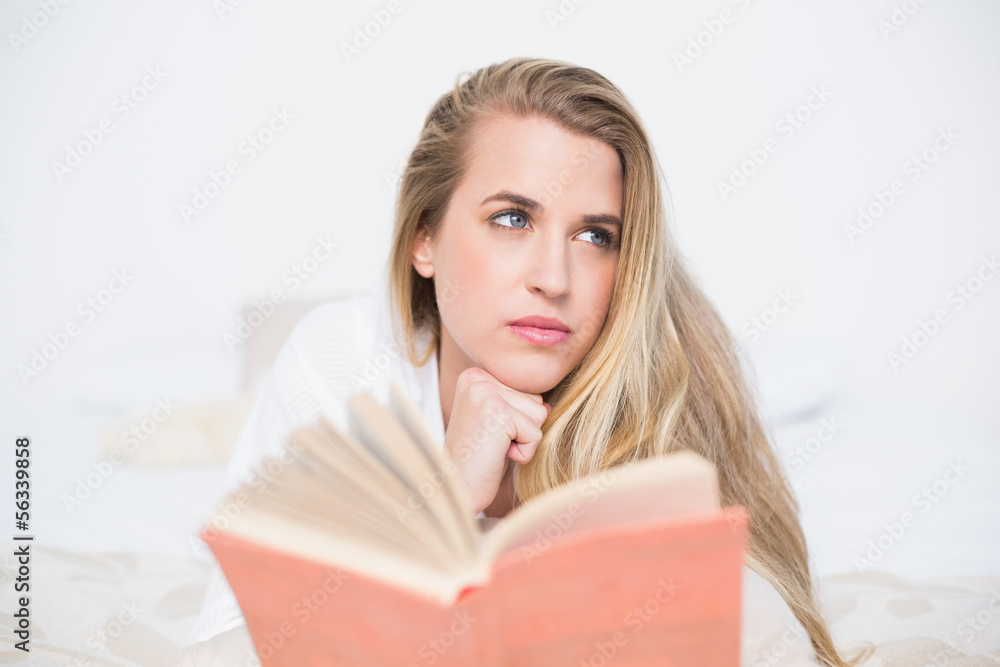 Pensive gorgeous model lying on cosy bed holding book Pensive gorgeous model lying on cosy bed holding book