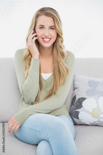 Happy pretty blonde on the phone sitting on cosy sofa