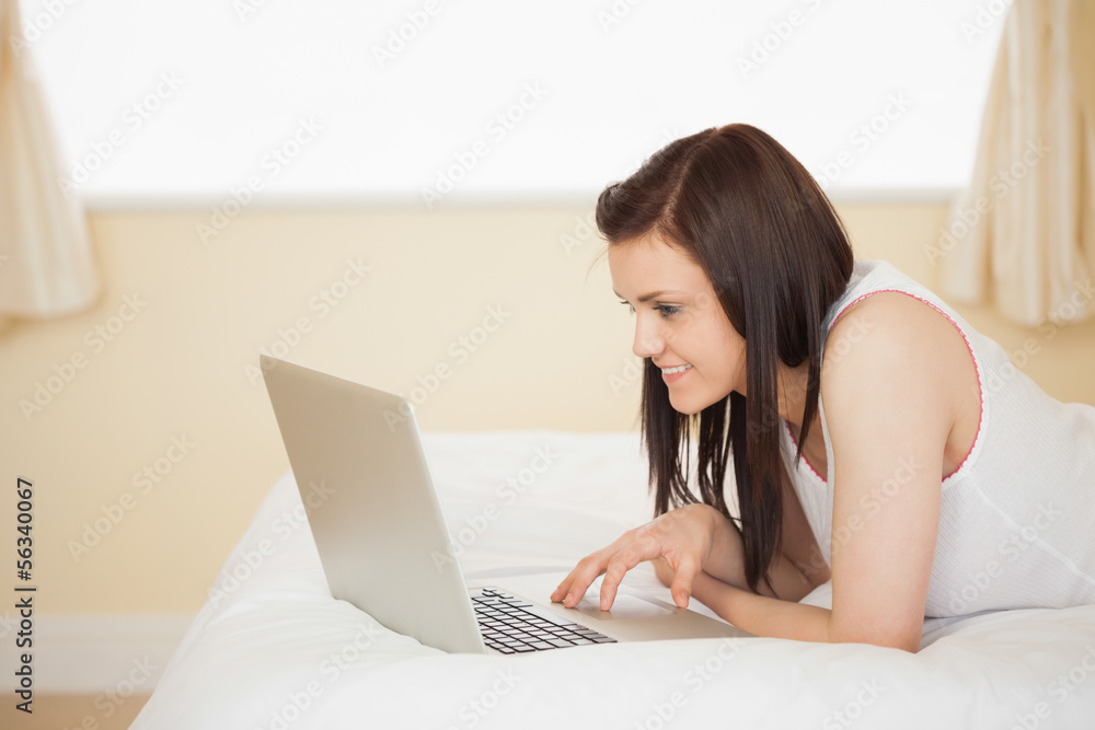 Cheerful girl using a laptop lying on her bed Cheerful girl using a laptop lying on her bed