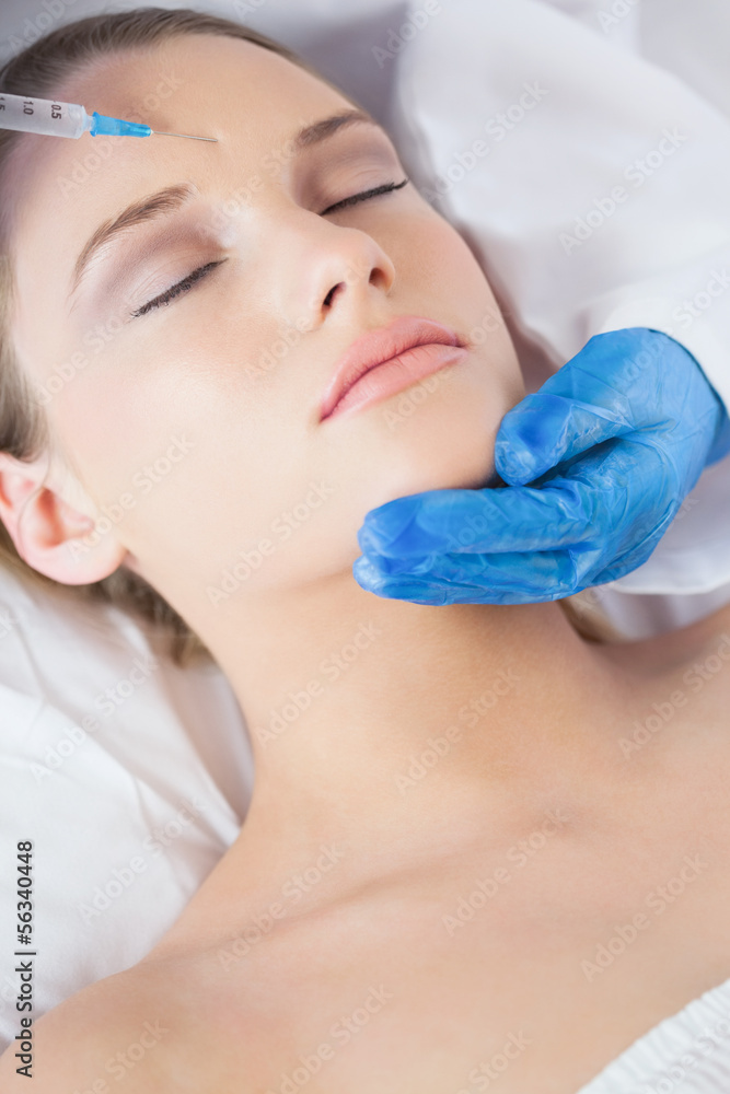 Surgeon making injection on forehead on peaceful woman lying Surgeon making injection on forehead on peaceful woman lying