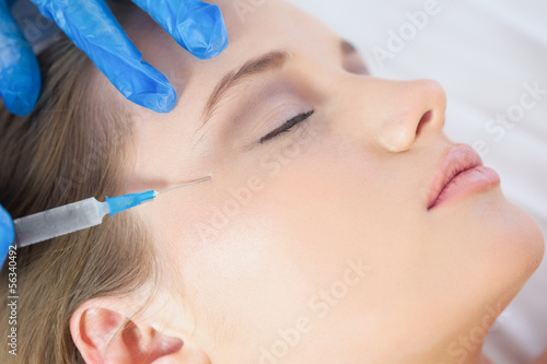 Surgeon giving injection to calm young woman's face