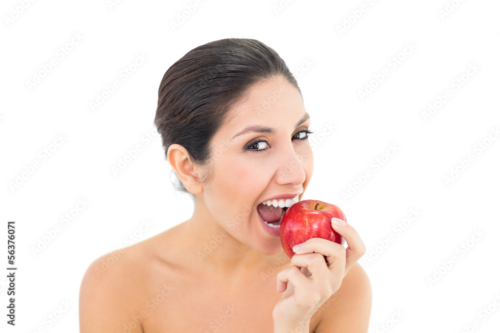 Happy brunette eating a red apple and looking at camera Happy brunette eating a red apple and looking at camera