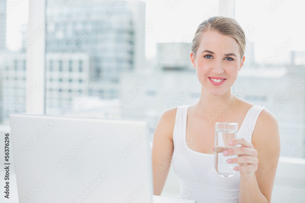 Cute blonde holding glass of water using her laptop Cute blonde holding glass of water using her laptop