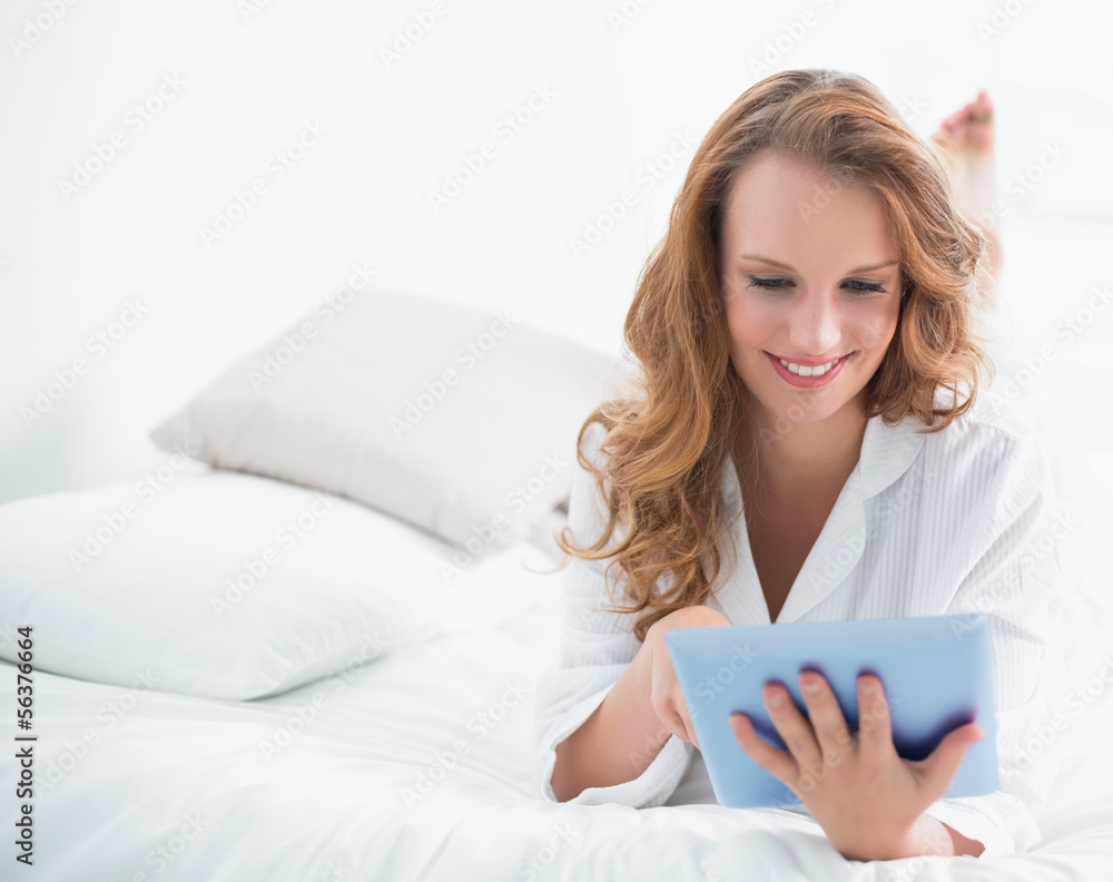 Cheerful pretty woman using a tablet pc lying on her bed Cheerful pretty woman using a tablet pc lying on her bed