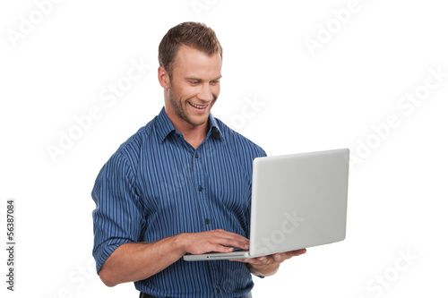 Man with laptop. Cheerful young man working on laptop and smilin