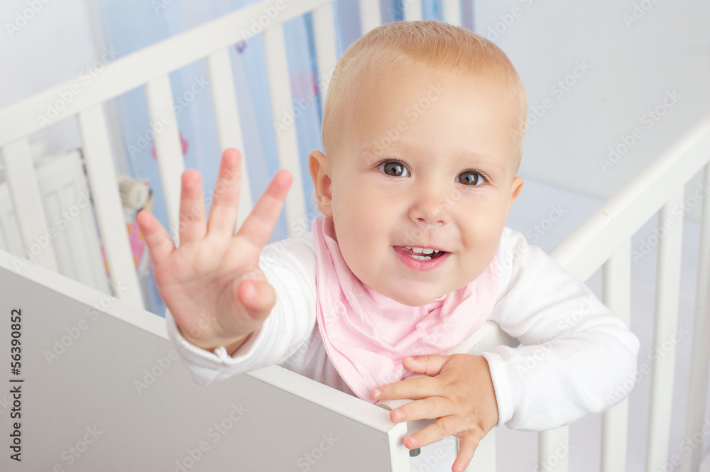 Portrait of a cute baby waving hello and smiling from crib Portrait of a cute baby waving hello and smiling from crib