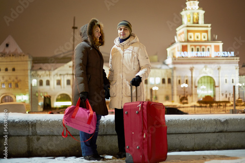 Young couple with big red trolley bag stands in evening © Pavel Losevsky