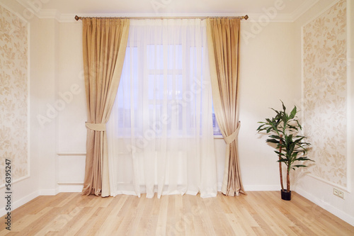 Window with beige curtains in simple room with plant on floor