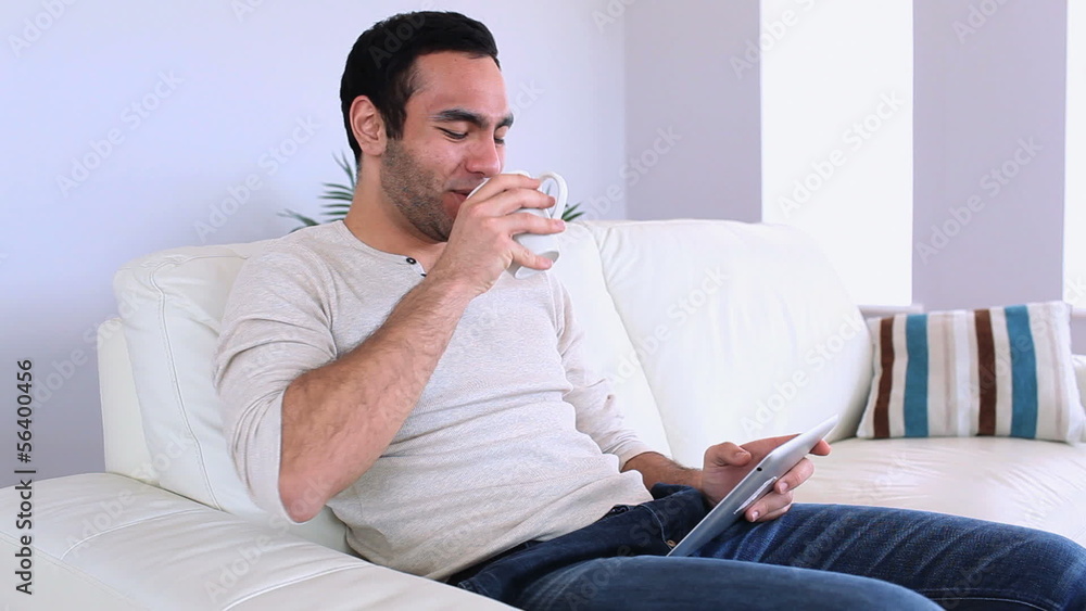 Handsome man using his tablet pc relaxing on his sofa Handsome man using his tablet pc relaxing on his sofa
