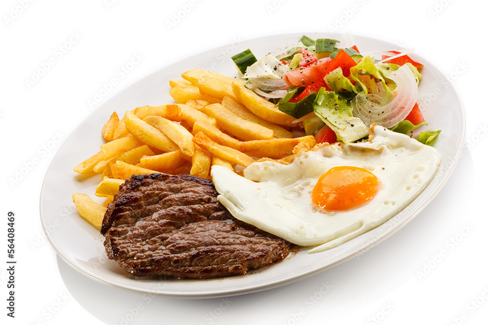 Grilled steaks, French fries, fried egg and vegetables Grilled steaks, French fries, fried egg and vegetables