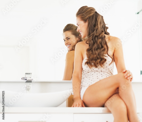 Happy young woman sitting in bathroom and looking in mirror