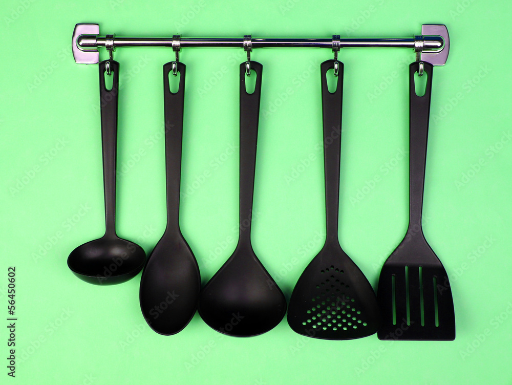 Black kitchen utensils on silver hooks, on green background Black kitchen utensils on silver hooks, on green background