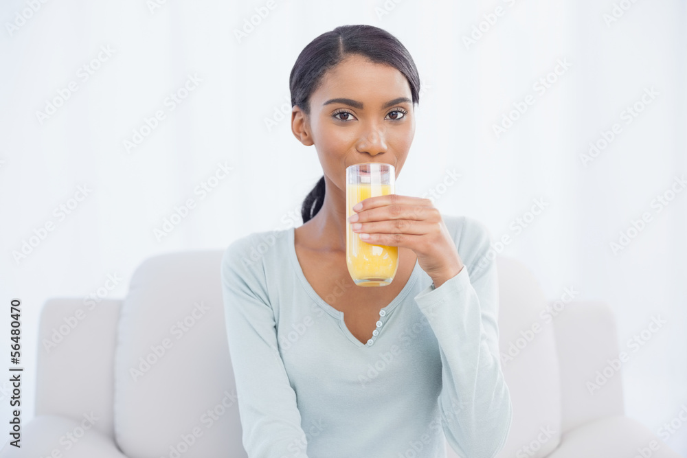 Smiling woman sitting on cosy sofa drinking orange juice Smiling woman sitting on cosy sofa drinking orange juice