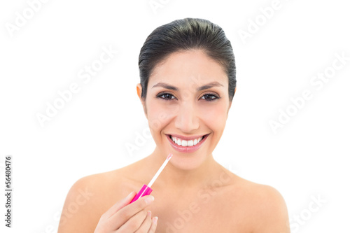 Brunette applying lip gloss and smiling at camera