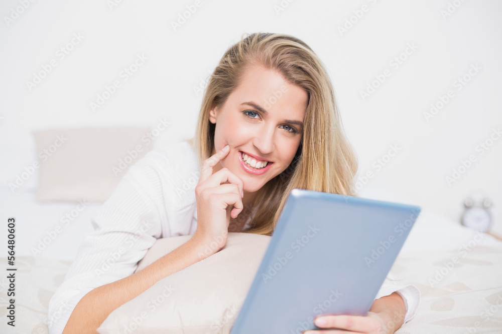 Smiling pretty model using her tablet lying on cosy bed Smiling pretty model using her tablet lying on cosy bed
