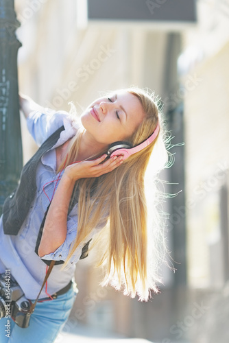 Happy hipster girl listening music on city street