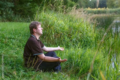 Young handsome  man sitting near forest lake and relaxing