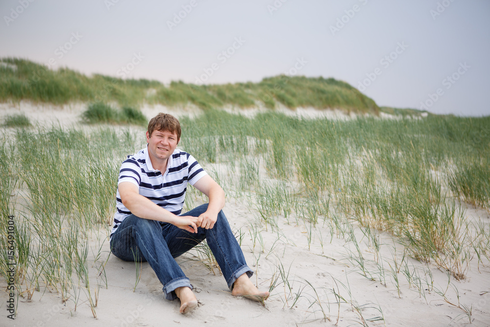 Young happy man relaxing on sand dunes of the beach of St.Peter