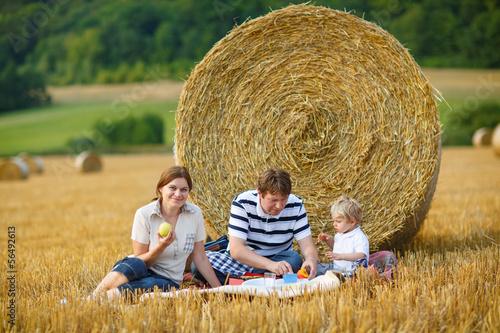 happy family of three picnicking on yellow hay field in summer. photo