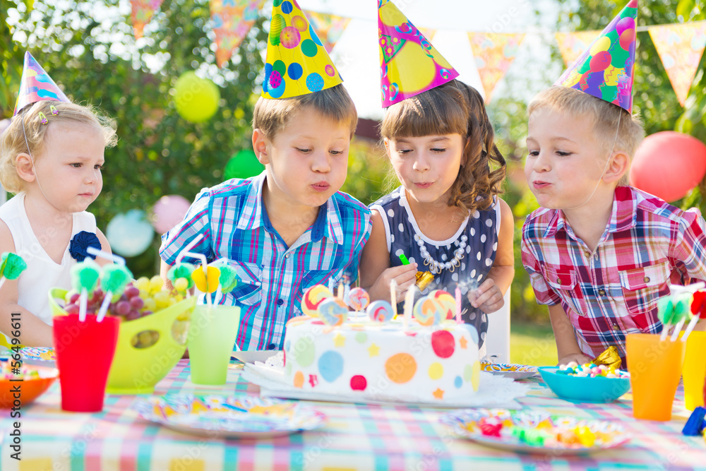 Kids blowing candles on cake at  birthday party - obrazy, fototapety, plakaty 
