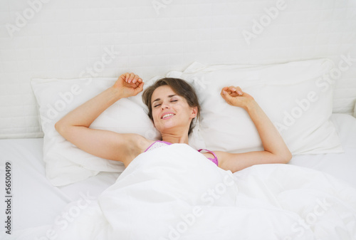 Happy young woman stretching in bed after sleep