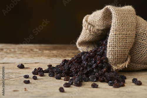 Black raisins in burlap bag over wooden table