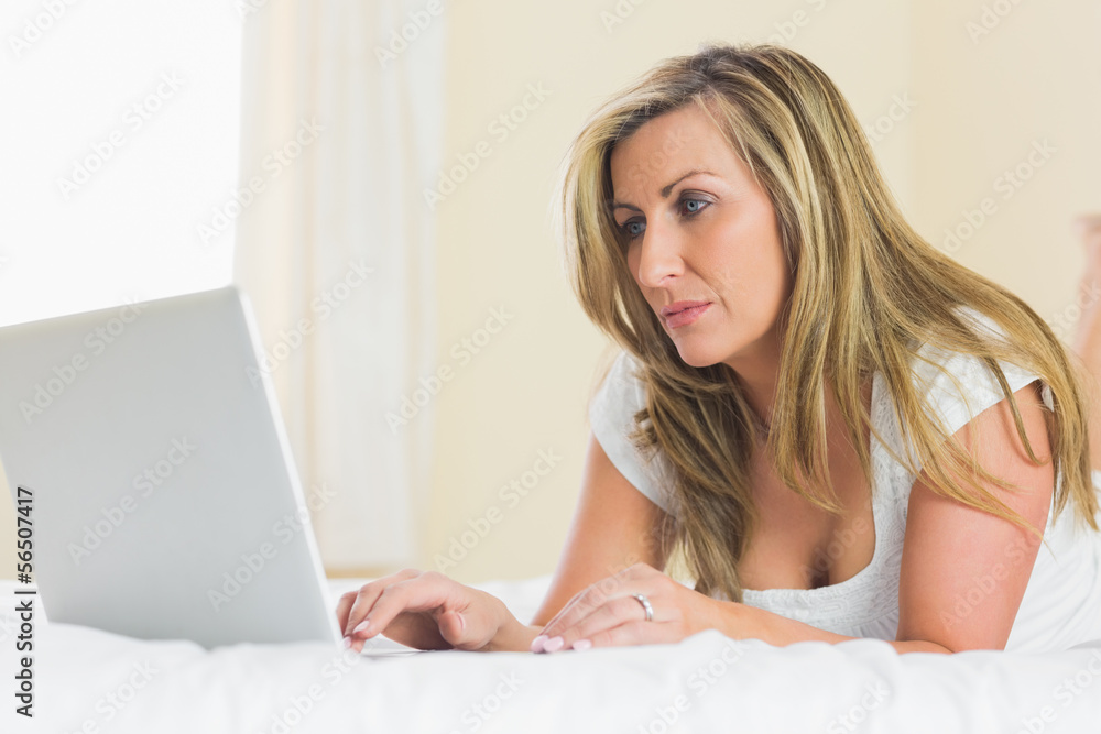 Concentrated woman using her laptop lying on her bed Concentrated woman using her laptop lying on her bed