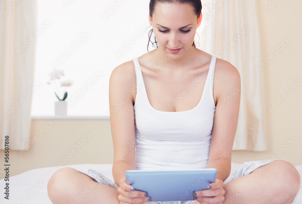 Content brunette sitting on bed using her tablet pc