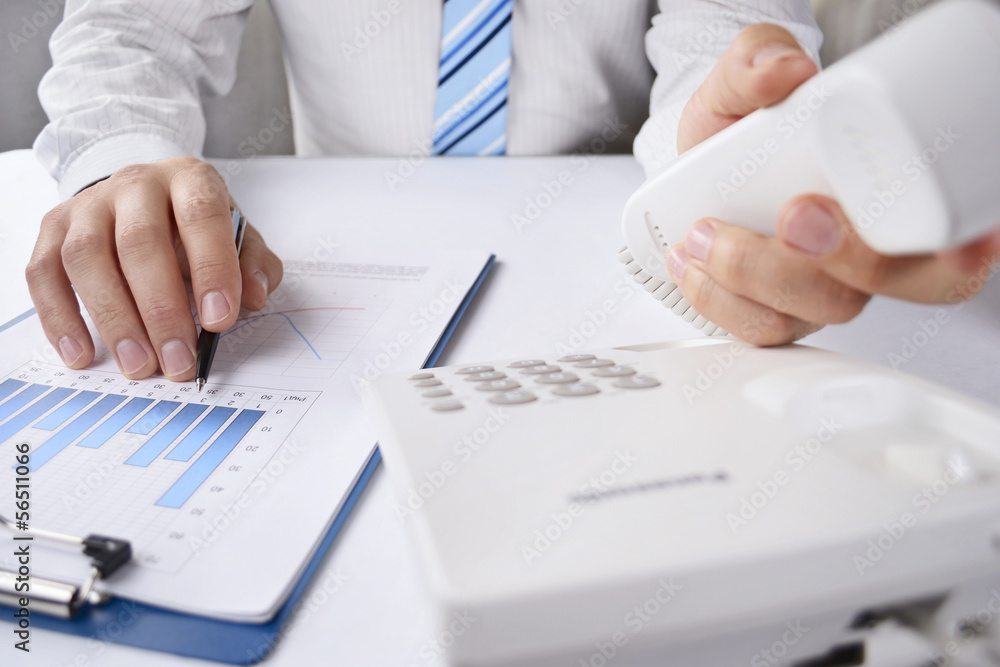 Man working at his desk reaching for the phone Man working at his desk reaching for the phone