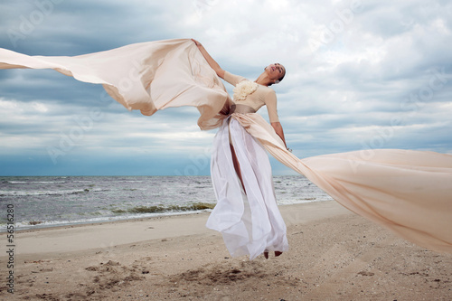 model jumps with long dress like a wings at the beach photo