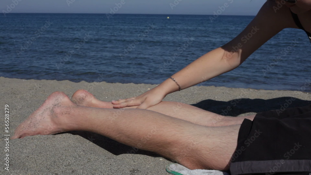 Female hand applying sun cream on male legs on the beach Female hand applying sun cream on male legs on the beach