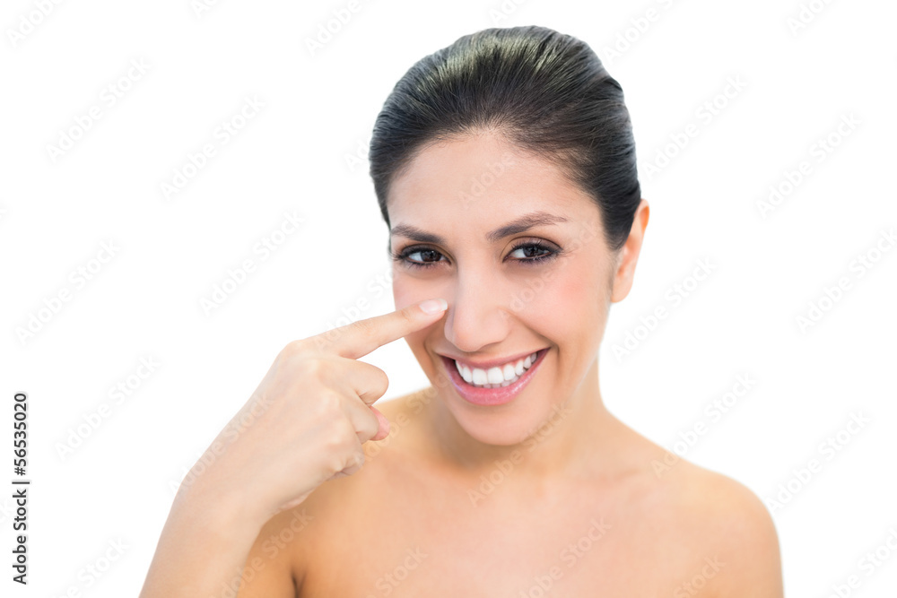 Smiling brunette pointing to nose and looking at camera