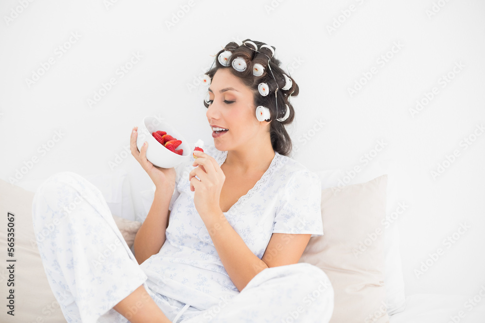 Smiling brunette in hair rollers having a bowl of strawberries Smiling brunette in hair rollers having a bowl of strawberries