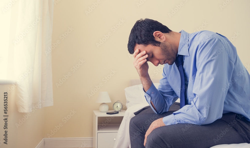 Depressed man sitting head in hands on his bed Depressed man sitting head in hands on his bed