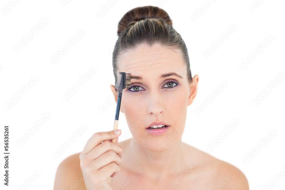 Woman brushing her eyebrow looking shocked at camera
