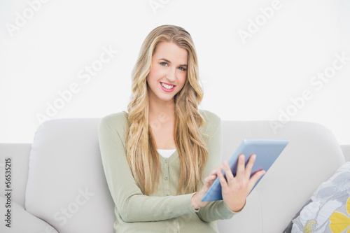 Cheerful pretty blonde using her tablet sitting on cosy sofa