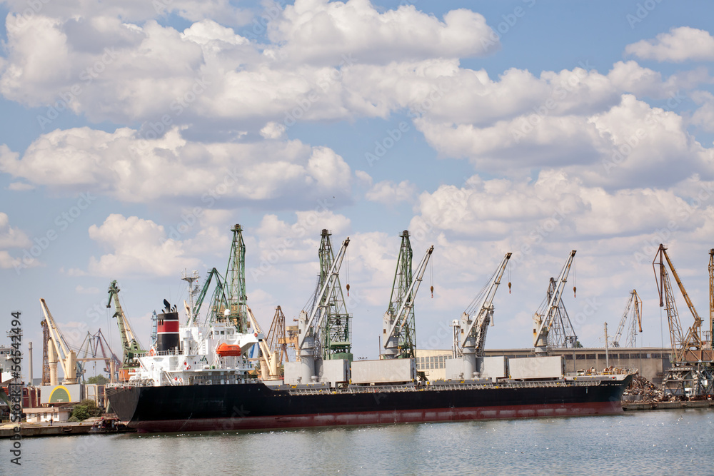 Large cargo ship in a dock at port. Cloudy sky