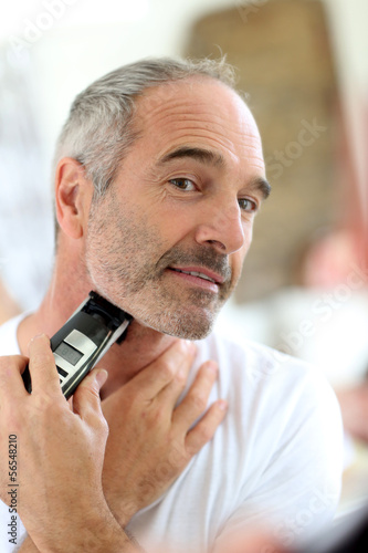 Senior man shaving beard with electric razor