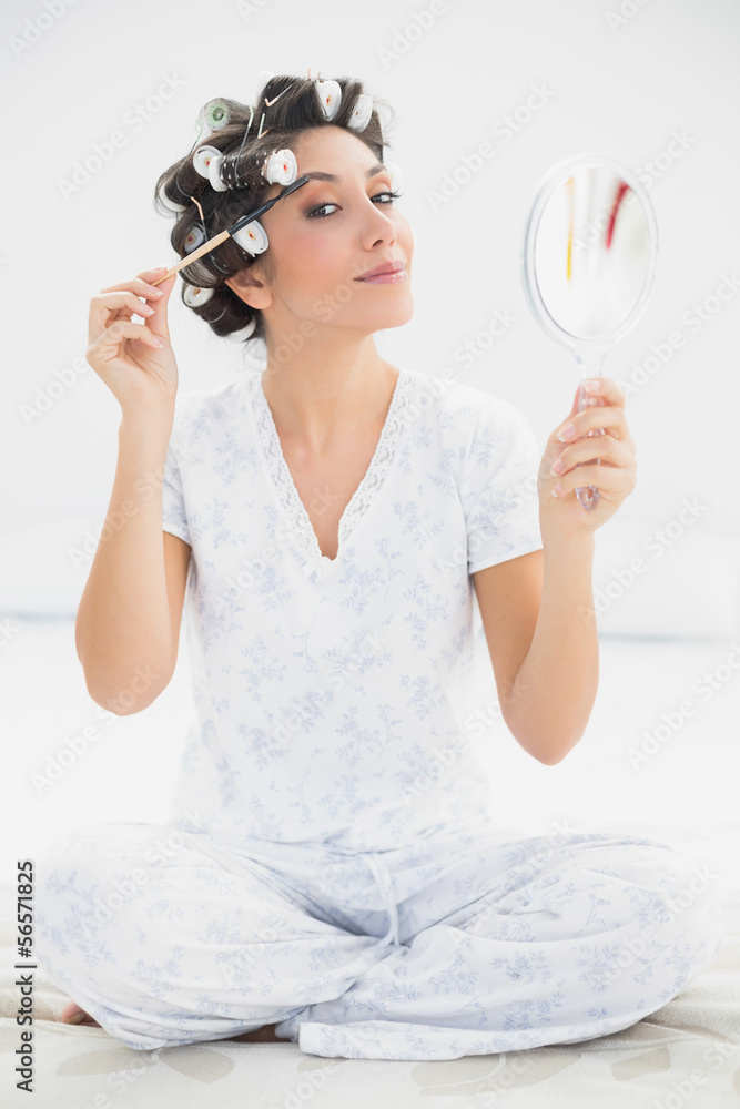 Happy brunette in hair rollers holding hand mirror and brushing Happy brunette in hair rollers holding hand mirror and brushing