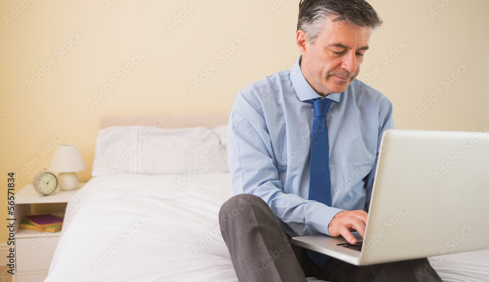 Concentrated man using a laptop sitting on a bed Concentrated man using a laptop sitting on a bed