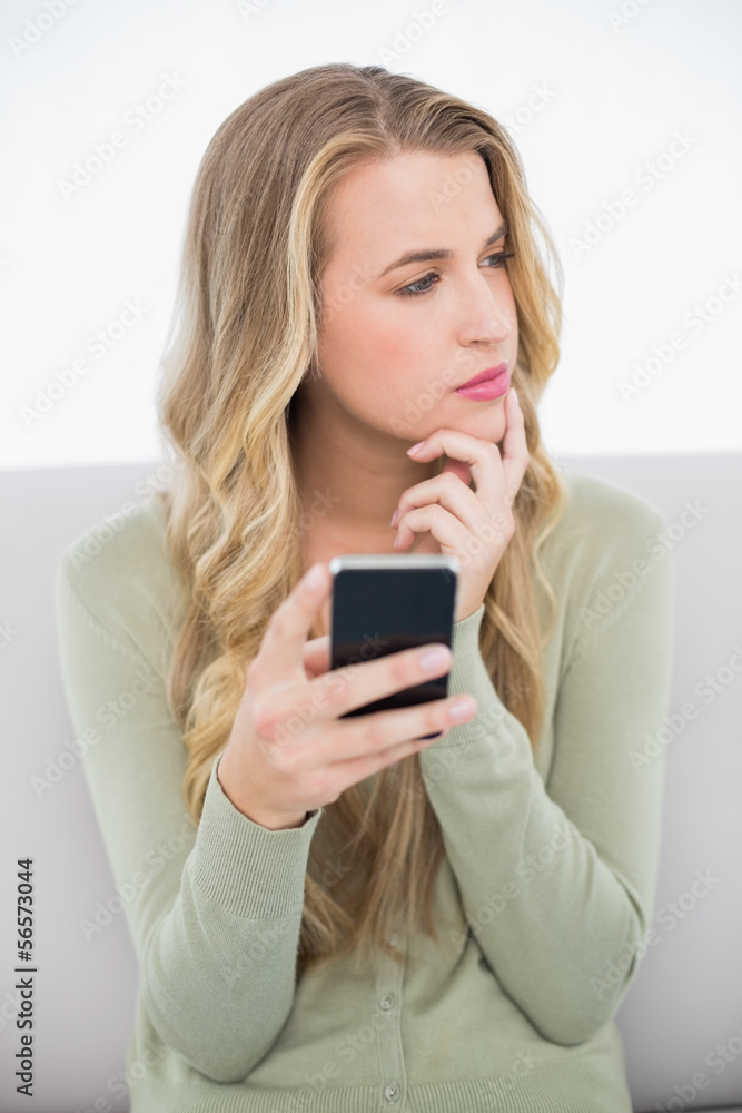 Pensive pretty blonde sending a text sitting on cosy sofa Pensive pretty blonde sending a text sitting on cosy sofa