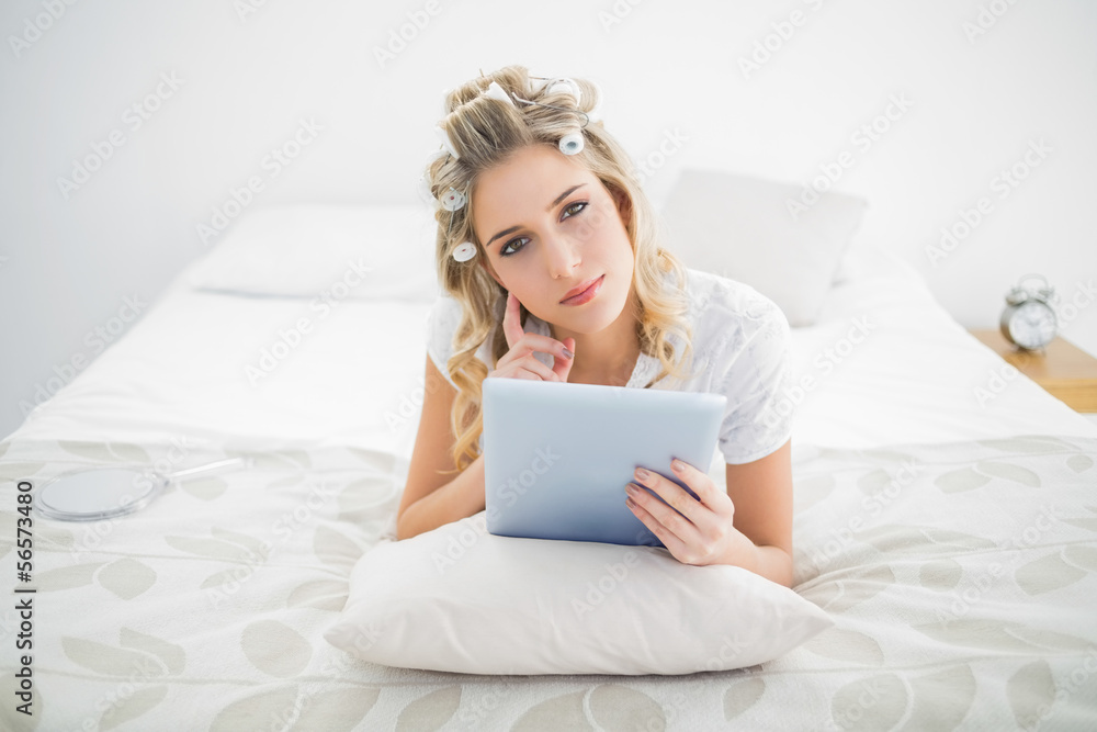 Thoughtful pretty blonde wearing hair curlers using tablet pc Thoughtful pretty blonde wearing hair curlers using tablet pc