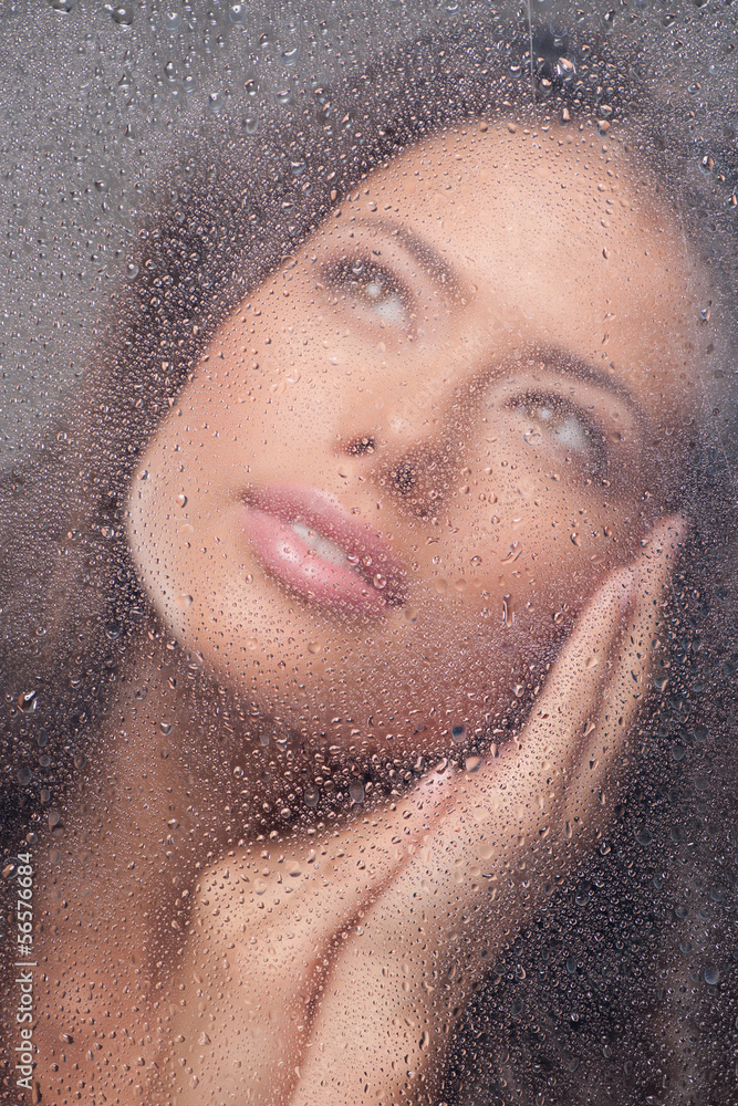 Girl dreaming. Beautiful young woman looking through wet window