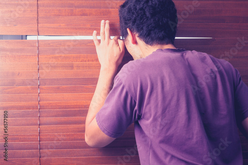 Tableau sur toile Young man peeping out through venetian blinds