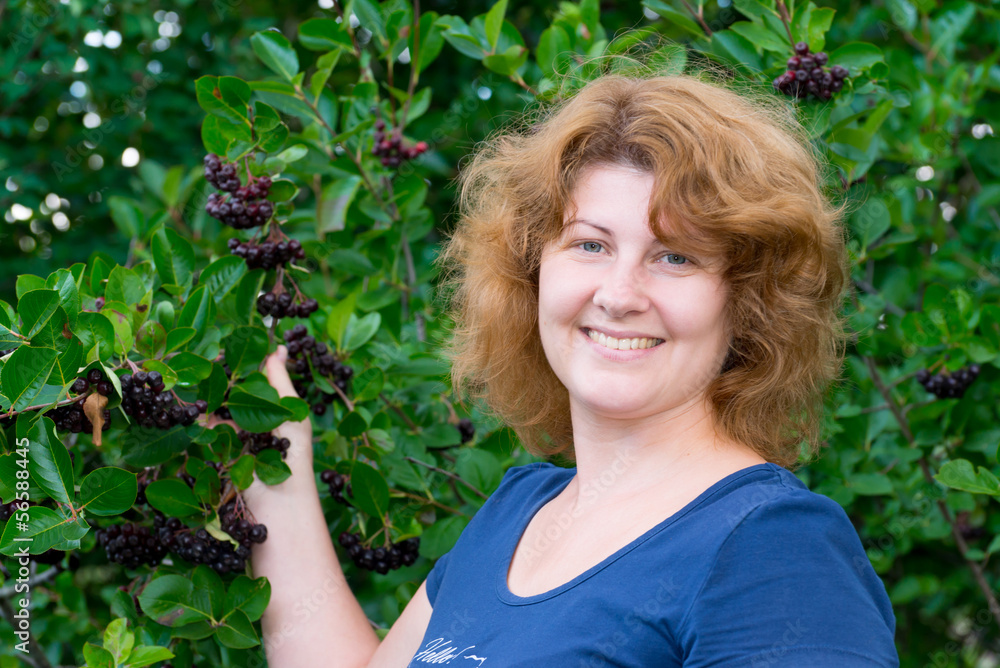 A woman in a black chokeberry bush in the garden A woman in a black chokeberry bush in the garden