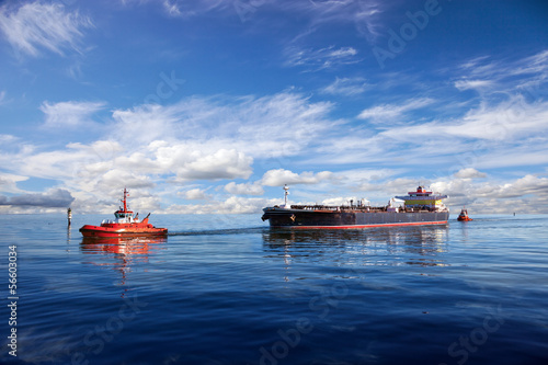 Tanker ship being guided into port by two tugs.