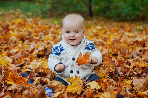 Child in knitted sweater sits among pumpkins in autumn park