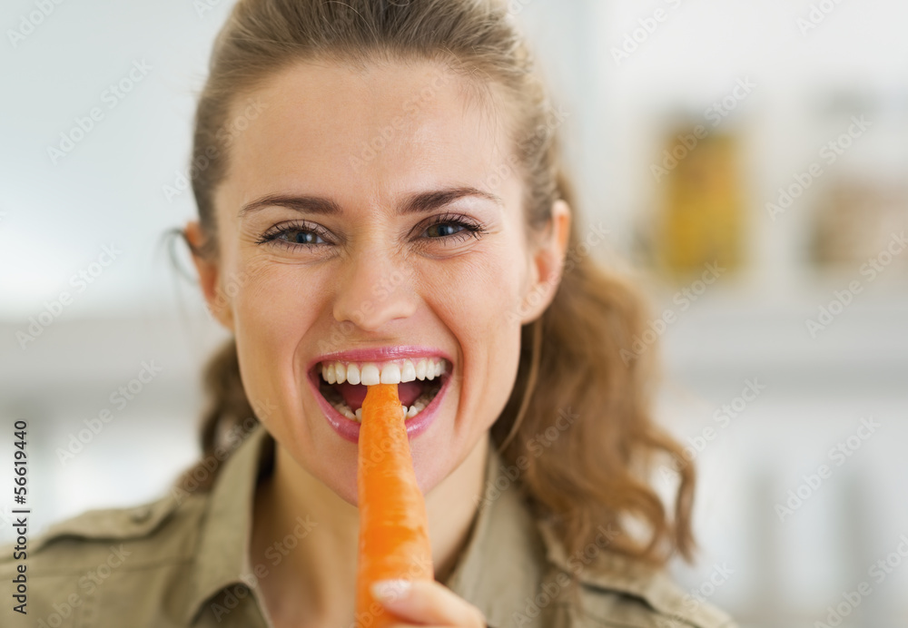 Happy young housewife eating carrot in kitchen Happy young housewife eating carrot in kitchen