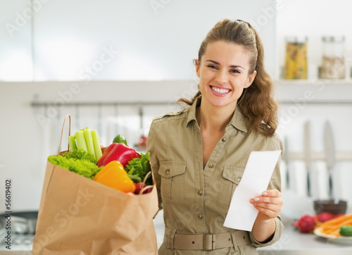 Smiling housewife with check and shopping bag full of vegetables