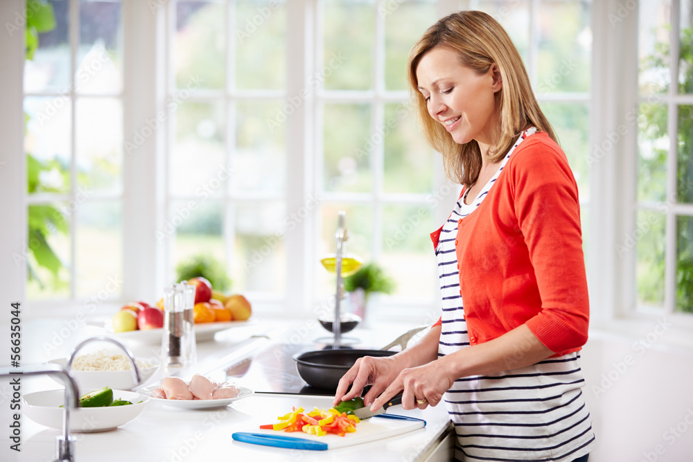 Woman Standing At Counter Preparing Meal In Kitchen Woman Standing At Counter Preparing Meal In Kitchen